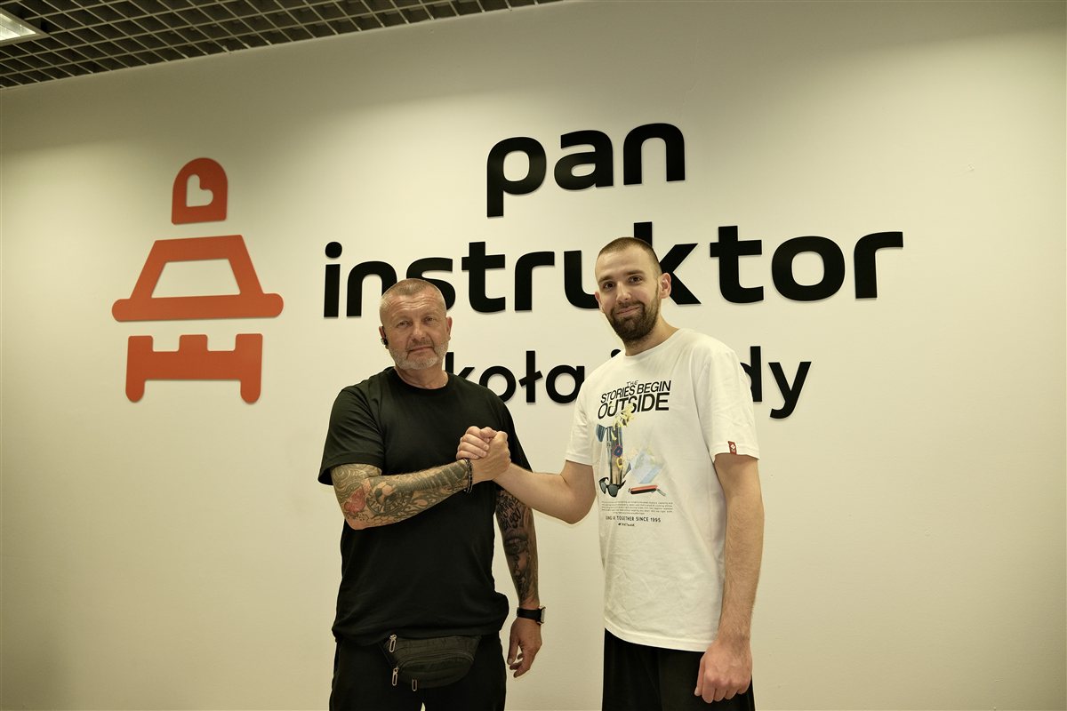 Instruktor i kursant przy ścianie z logo Pan Instruktor szkoła jazdy Warszawa